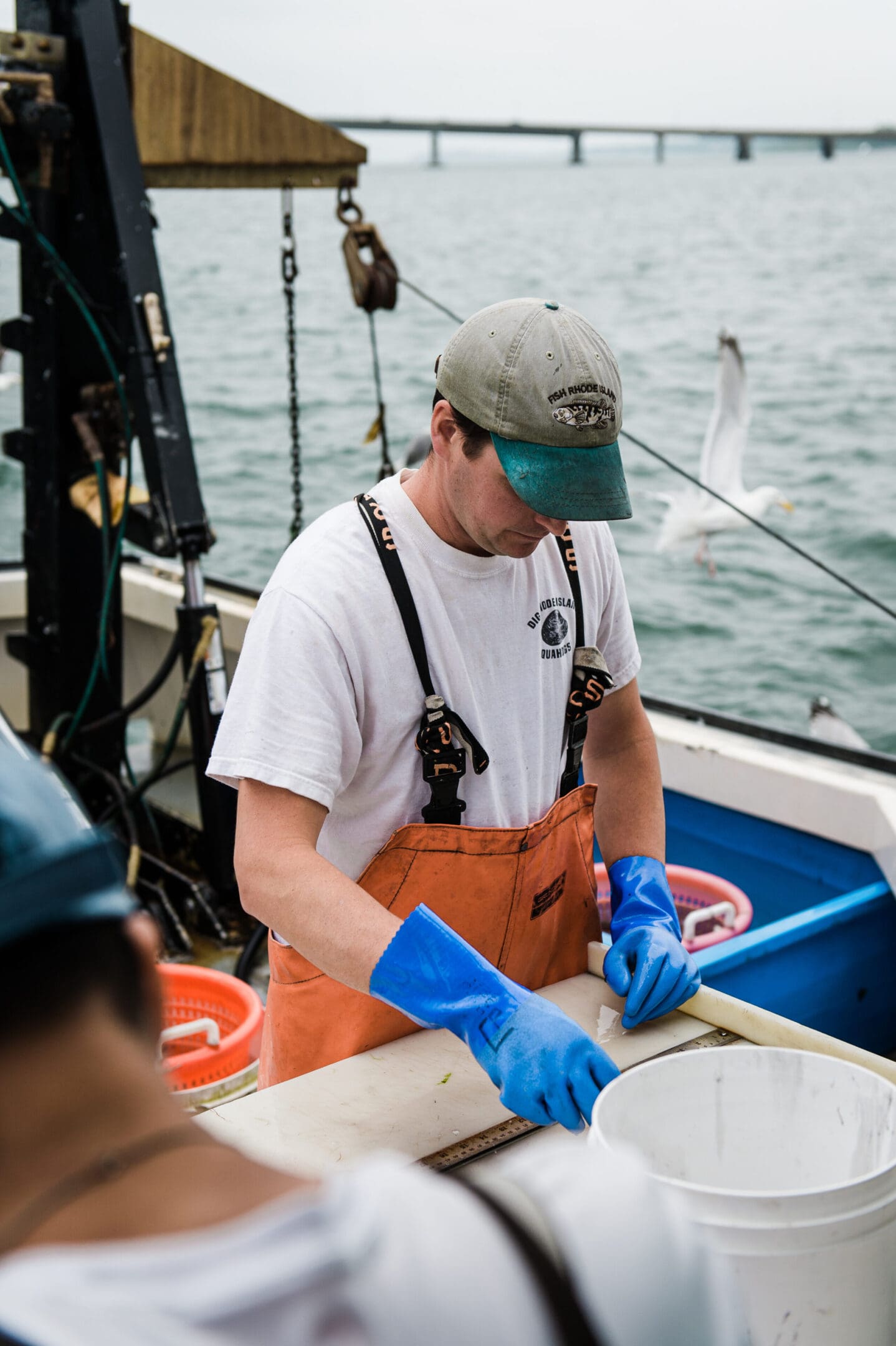 A man in an orange bib and blue gloves on a boat.